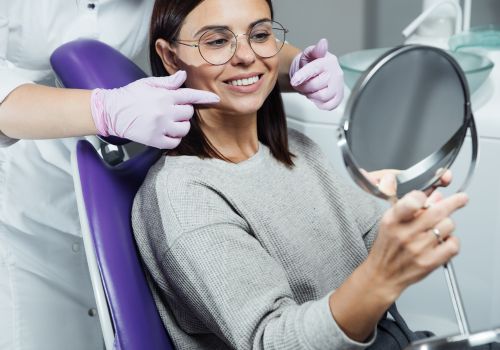 Female patient at dentists office looking handheld mirror to admire their smile